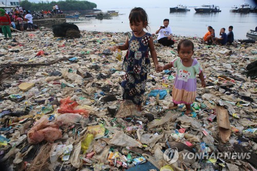 2019년 2월 21일 인도네시아 람풍주 반다르 람풍 시 해변에서 쓰레기 청소 행사가 진행 중인 가운데 어린이들이 바닥을 메운 플라스틱 쓰레기 위를 걷고 있다. [AFP=연합뉴스 자료사진]
