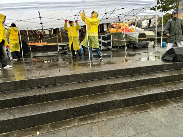 비가 오는 3일 공연을 위해 우비를 입고 천막을 치고 있는 자원가들.
