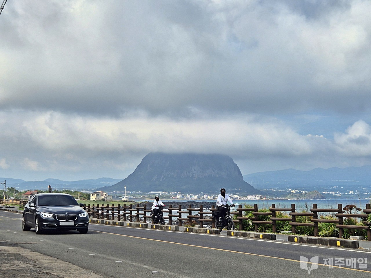 1일 서귀포시 상모리 형제해안도로를 달리는 자전거와 자동차 너머로 구름모자를 쓴 산방산이 보인다. [사진=조문호 기자]